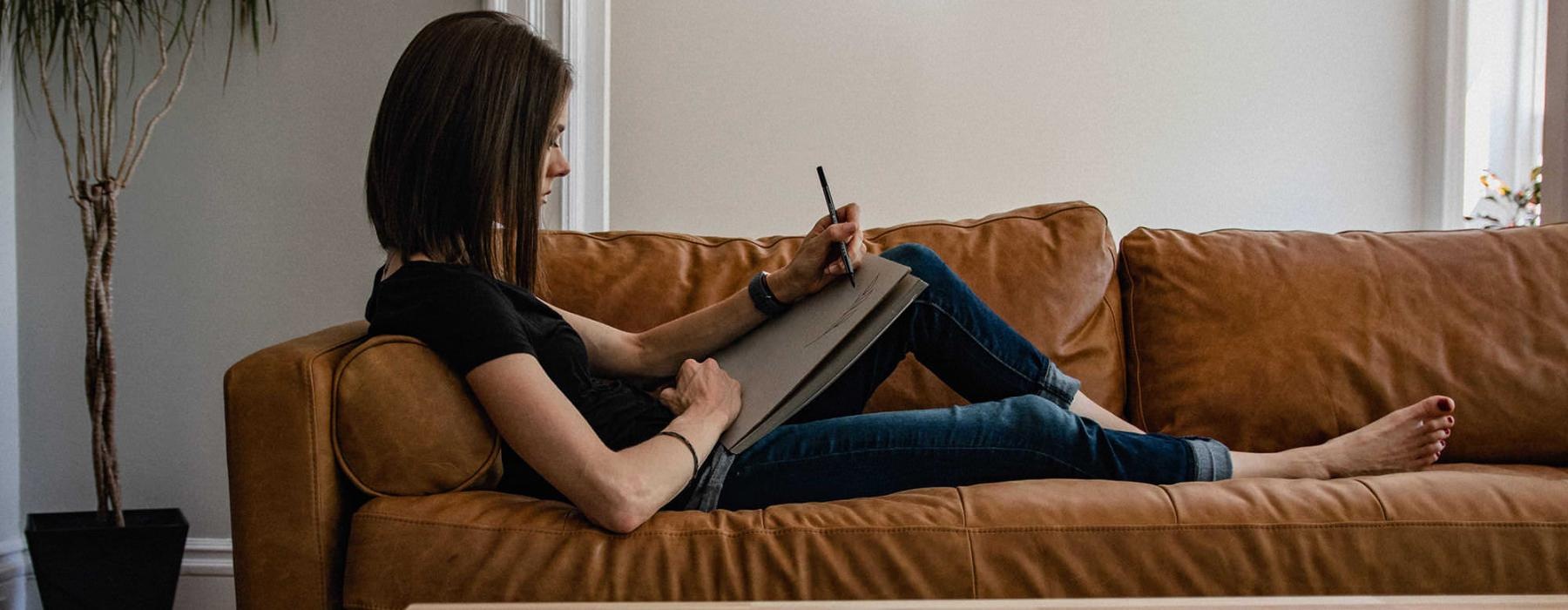 woman lies on a couch and draws on a large sketch pad